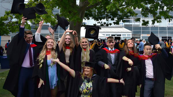 Un grupo de graduados en togas se reúne frente a un edificio en el campus del Worthing College.