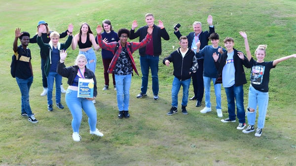 Estudiantes y adultos están juntos en un campo en el terreno del Worthing College y saludan con los brazos.