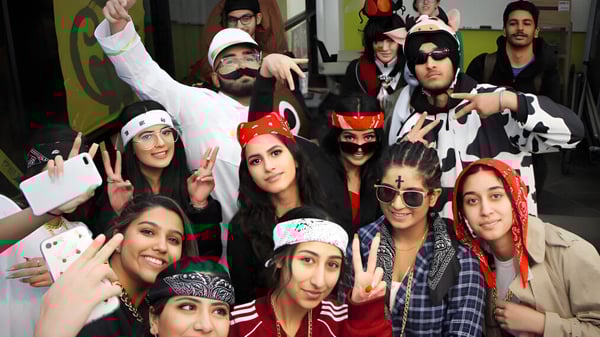 Un grupo de estudiantes de la W.P. Wagner High School posa en varios disfraces frente a un fondo colorido.