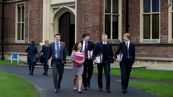 Un grupo de estudiantes bien vestidos camina por el campus del Wrekin College pasando junto a un edificio de ladrillo y una superficie de césped.