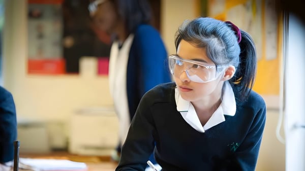 Una joven en traje negro y gafas está concentrada en una sala desordenada de la Wychwood School.