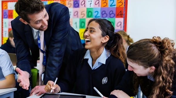 Alumnos de la Wycombe Abbey School discuten en el aula con su docente frente a coloridos paneles educativos.