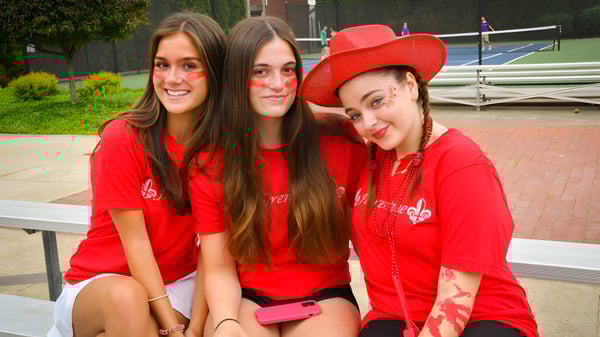 Tres estudiantes de Wyoming Seminary College Preparatory posan sonriendo juntas en el exterior frente a un edificio con plantas verdes.