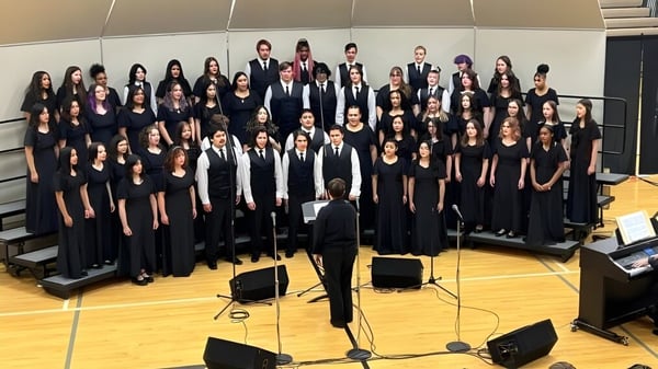Un gran coro de la Wyoming High School está en el escenario y canta bajo la dirección de un director.