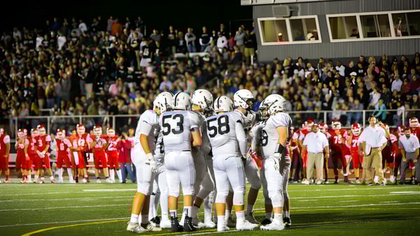 Un grupo de jugadores de fútbol de la Xavier High School está reunido en el campo frente a una gran multitud.