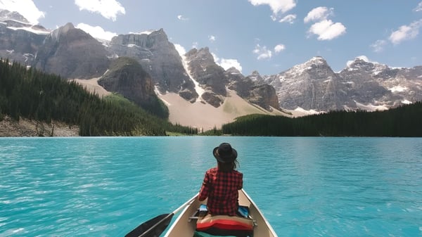 Una persona está en una pequeña barca en el tranquilo lago frente a montañas cubiertas de nieve en el terreno de la Yale Secondary School.