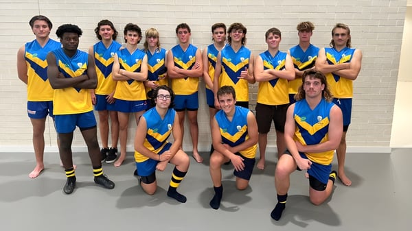 Un grupo de alumnas y alumnos del Yanchep Secondary College están juntos frente a una pared blanca en uniformes escolares azules y amarillos.