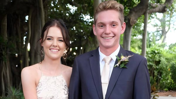 Una joven pareja está sonriendo en un área verde al aire libre en el terreno de la Yeppoon State High School.